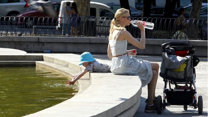 Una mujer bebiendo de una botella de agua con su hijo en una fuente
