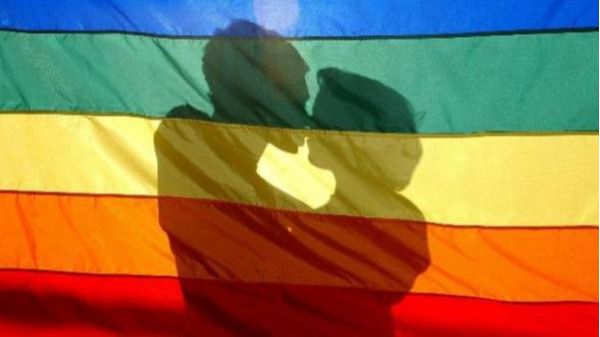 Pareja besandose detrás de la bandera LGTBI 