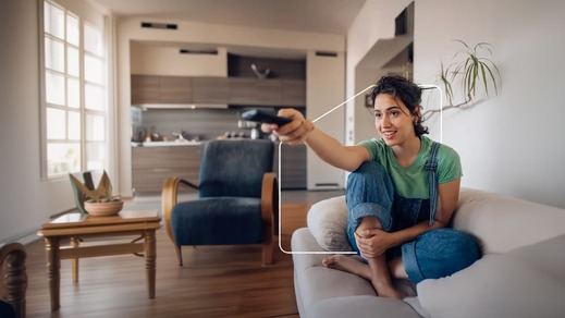 Una mujer sentada en su sofá cambia de canal de televisión desde el salón de su casa